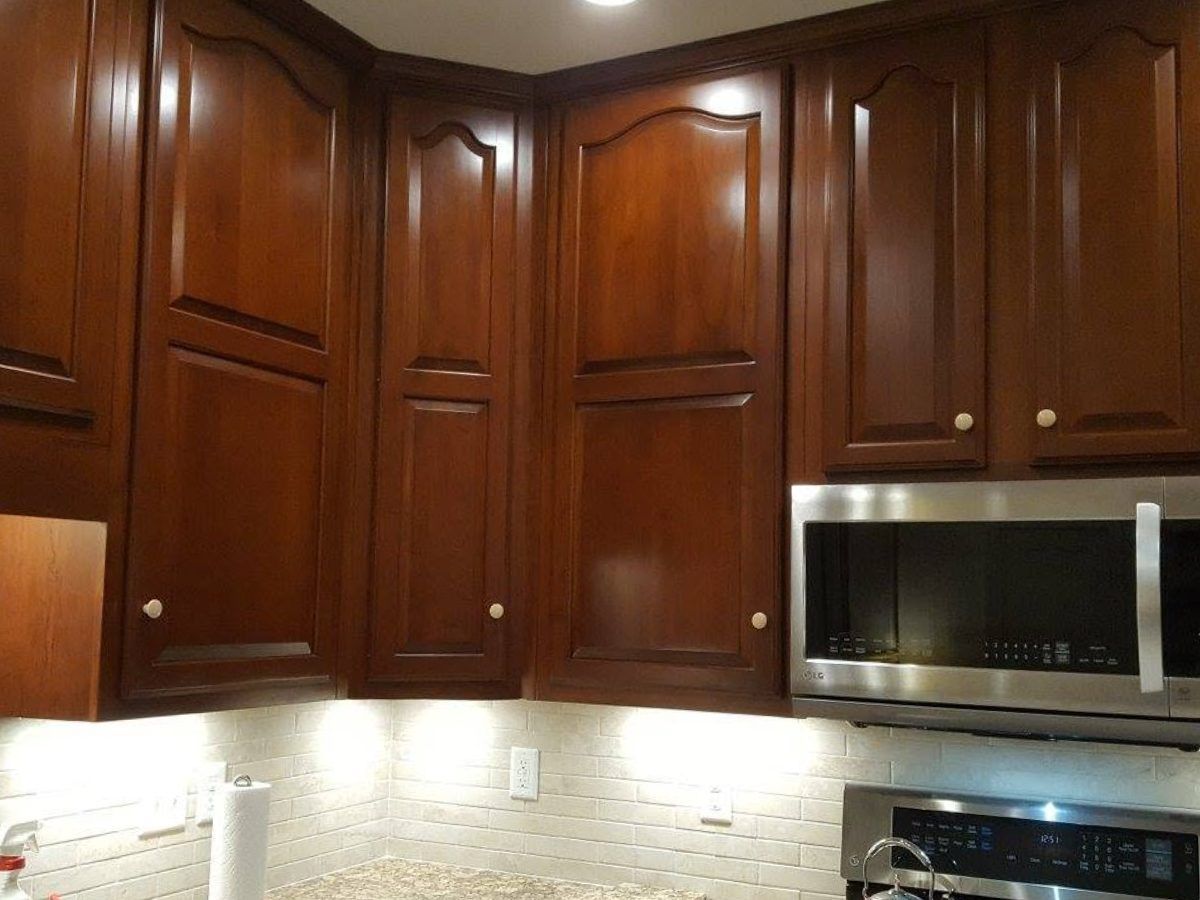 Refinished cherry kitchen cabinets with raised panel doors, wrapping a corner above a tiled floor.