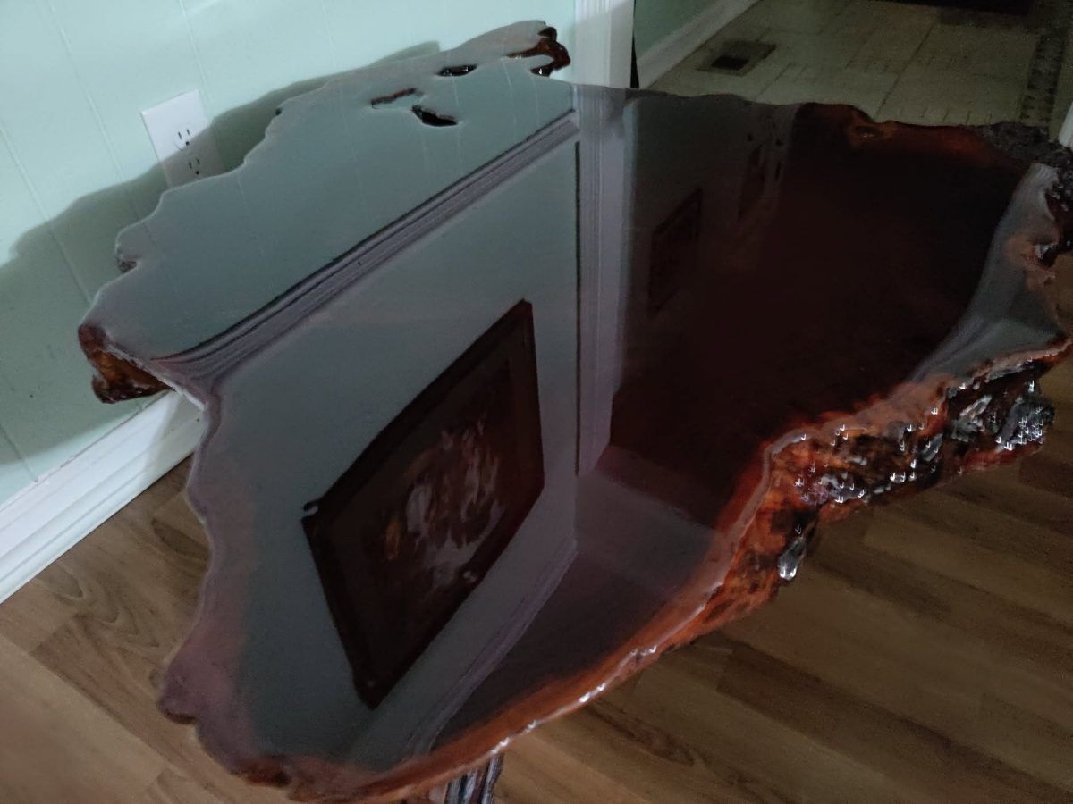 A live-edge slab table finished with a clear epoxy pour, the surface deep enough to reflect the wall and floor of the room.
