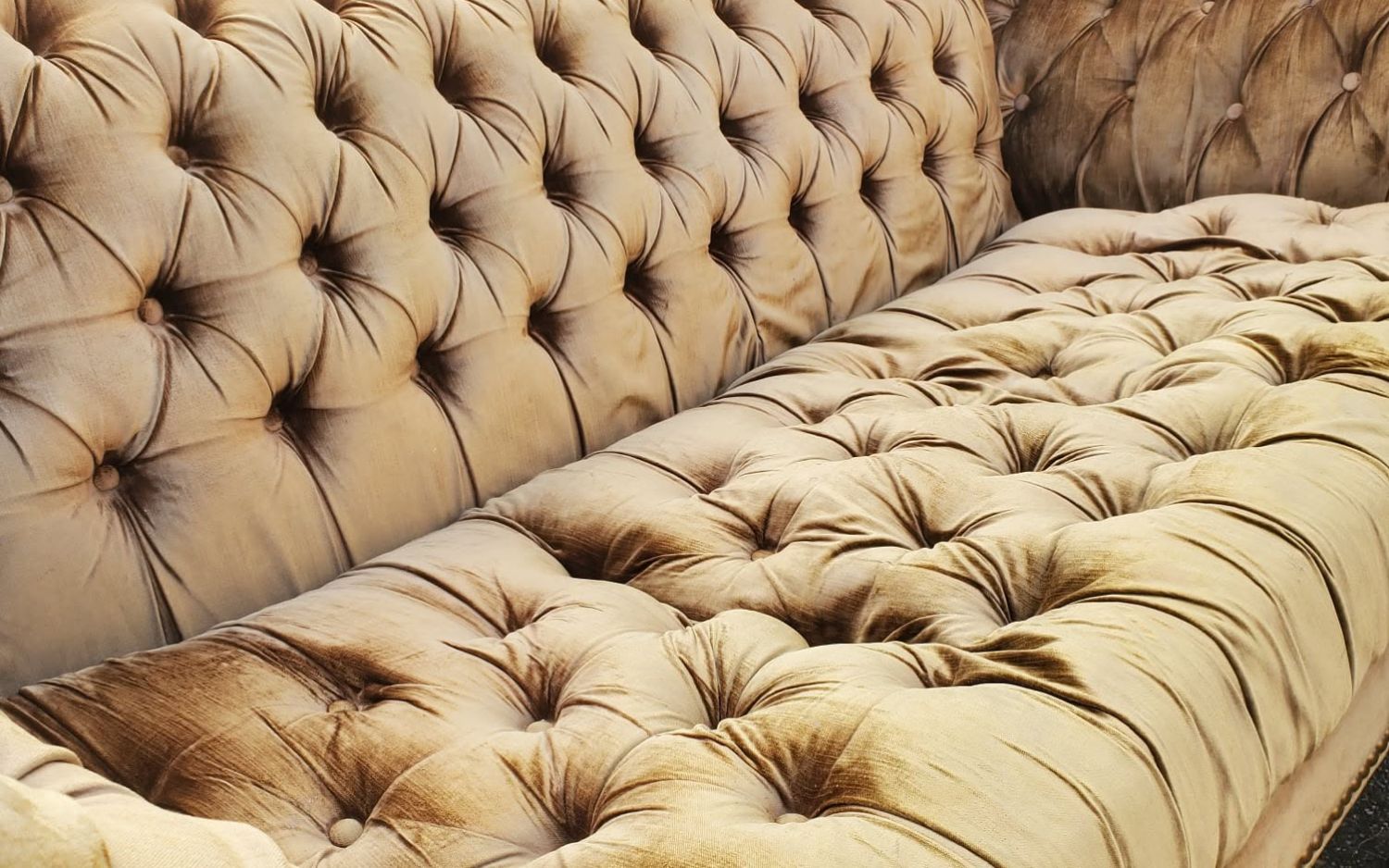 A deep-buttoned velvet sofa in the workshop, its buttons replaced and its cushion resecured.