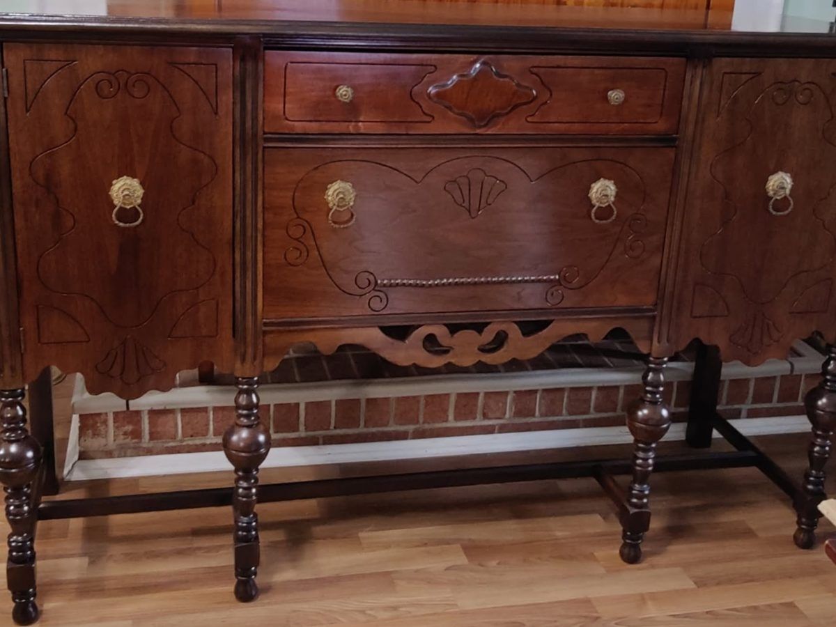 A refinished mahogany sideboard with carved panels, ring pulls and turned legs, standing on a wooden floor.