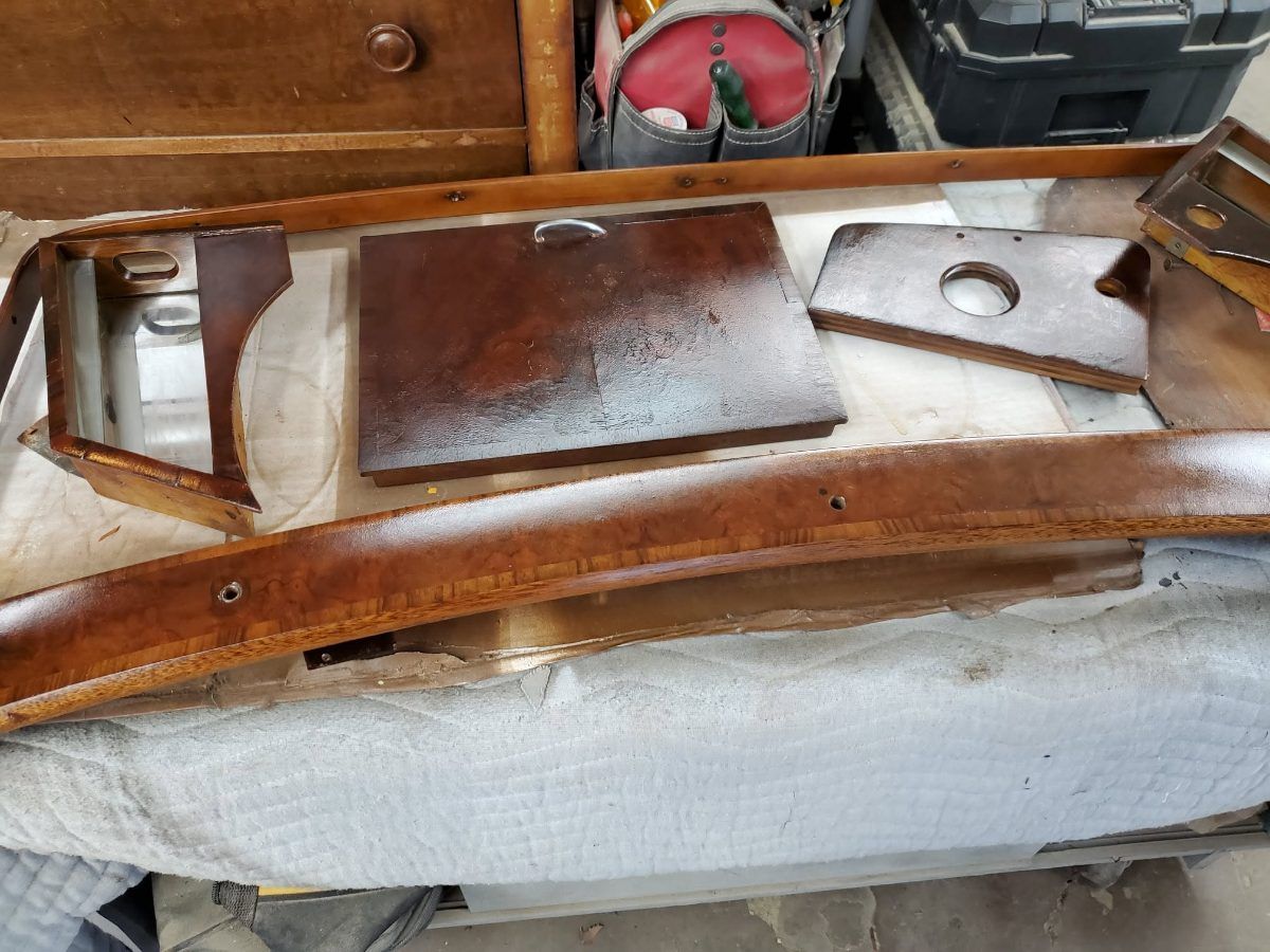 Burr walnut interior trim from an antique Bentley laid out on the bench — a long curved capping rail, a fascia panel drilled for an instrument, and two smaller pieces, partway through refinishing.