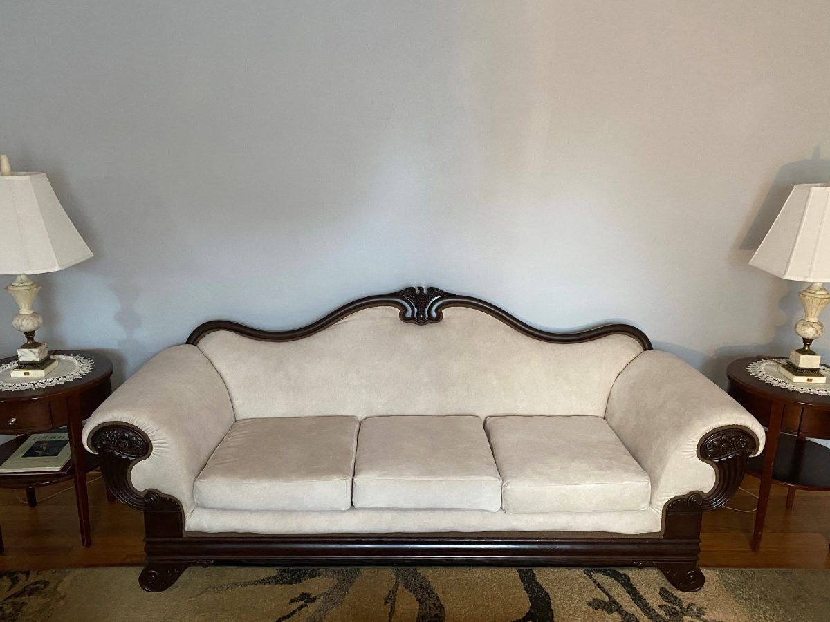 A Victorian sofa after reupholstery, covered in cream fabric with its carved and polished mahogany frame.