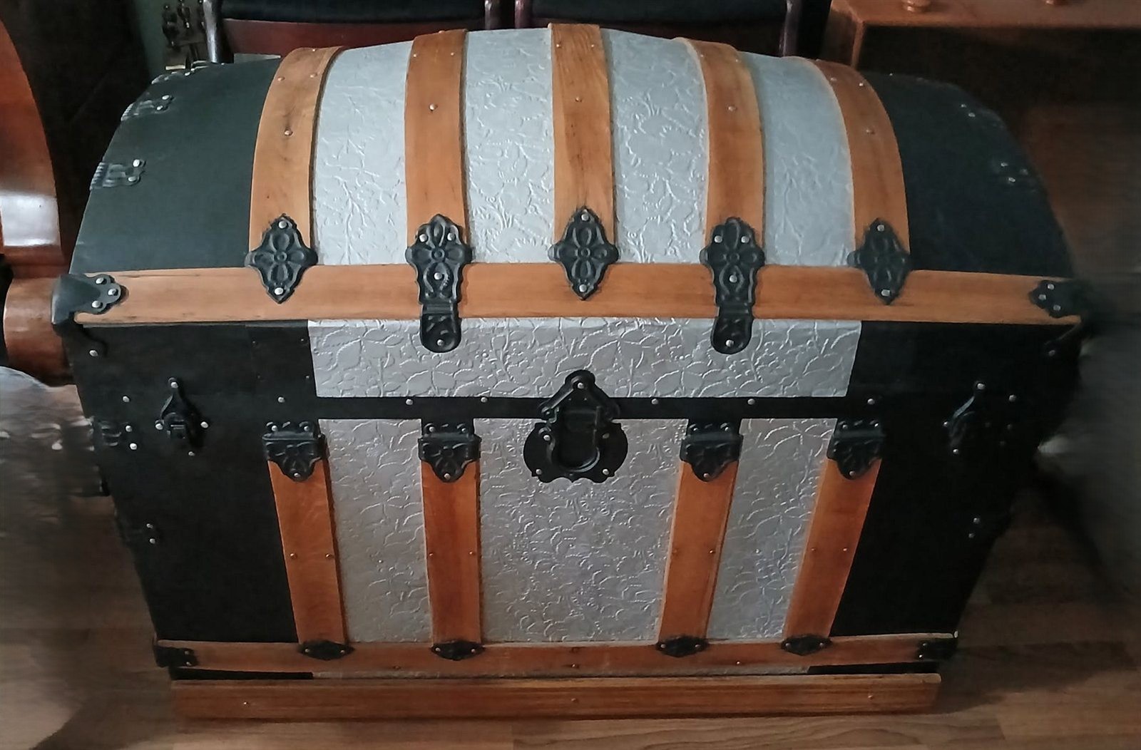 A restored Victorian dome-top steamer trunk with refinished oak slats, repainted embossed metal panels and original cast-iron hardware.